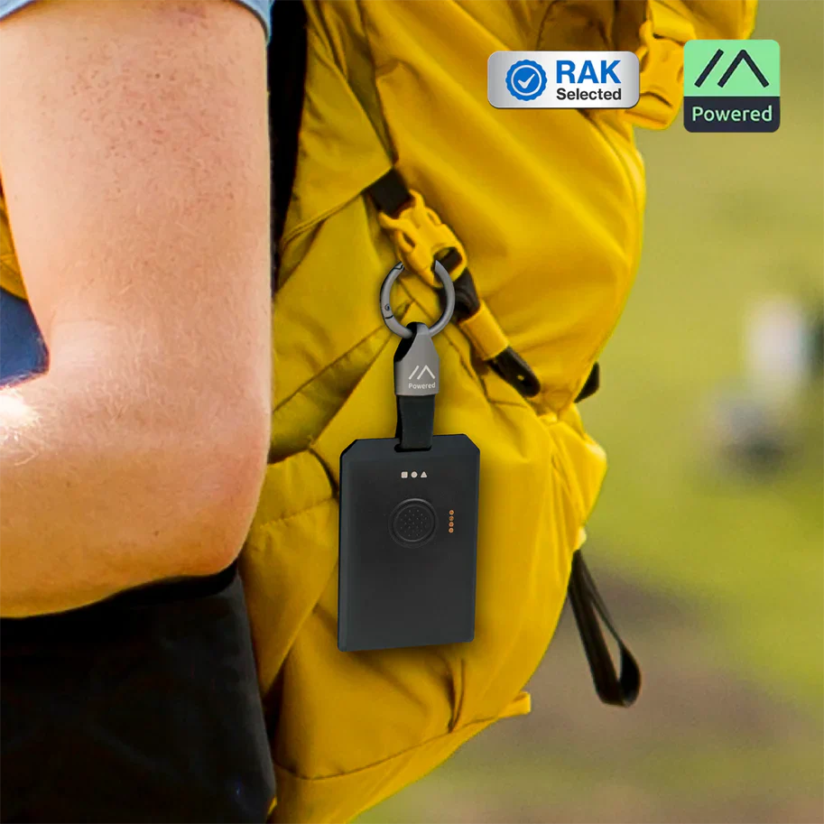 Meshtastic node attached to a hiker's backpack strap next to a smartphone displaying the Meshtastic messaging app.