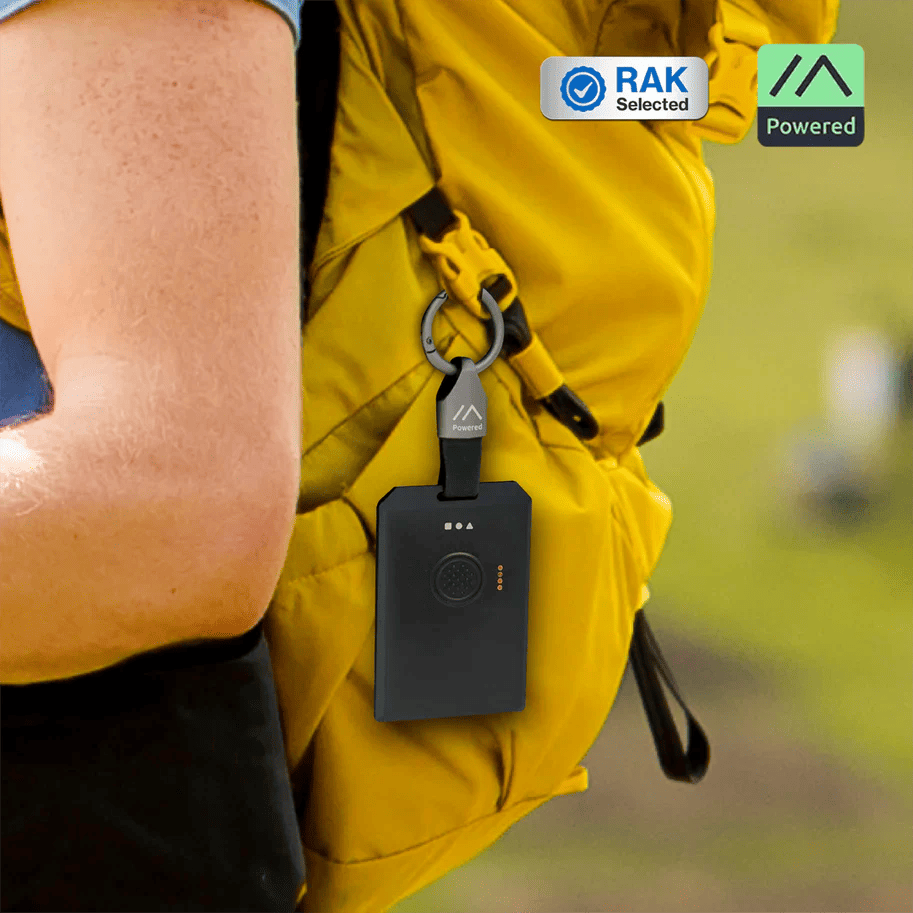 Meshtastic node attached to a hiker's backpack strap next to a smartphone displaying the Meshtastic messaging app.